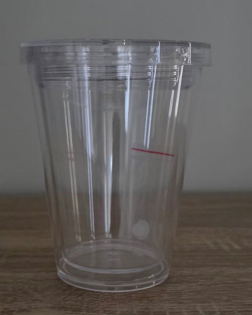 A clear plastic cup with a matching clear lid, sitting on a wooden surface against a neutral gray background.
BH Creations By Mel