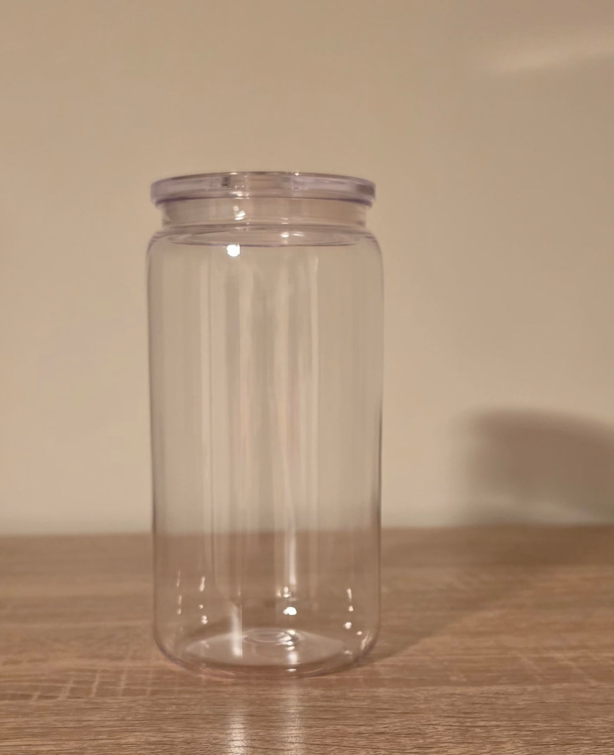 A clear plastic storage jar with a screw-on lid, standing on a wooden surface against a plain beige wall.
BH Creations by mel