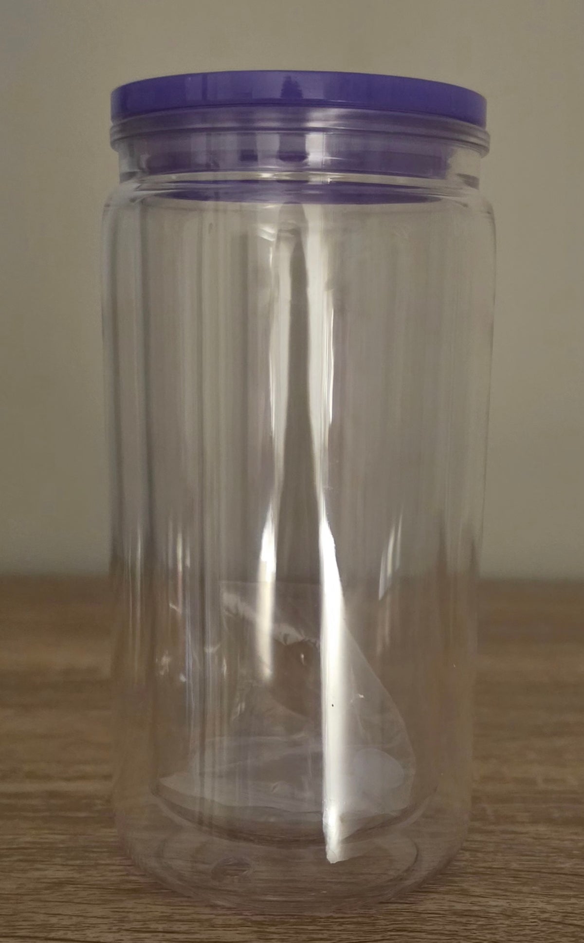 A clear plastic jar with a purple screw-on lid, standing on a wooden surface against a plain beige wall.
BH Creations By Mel