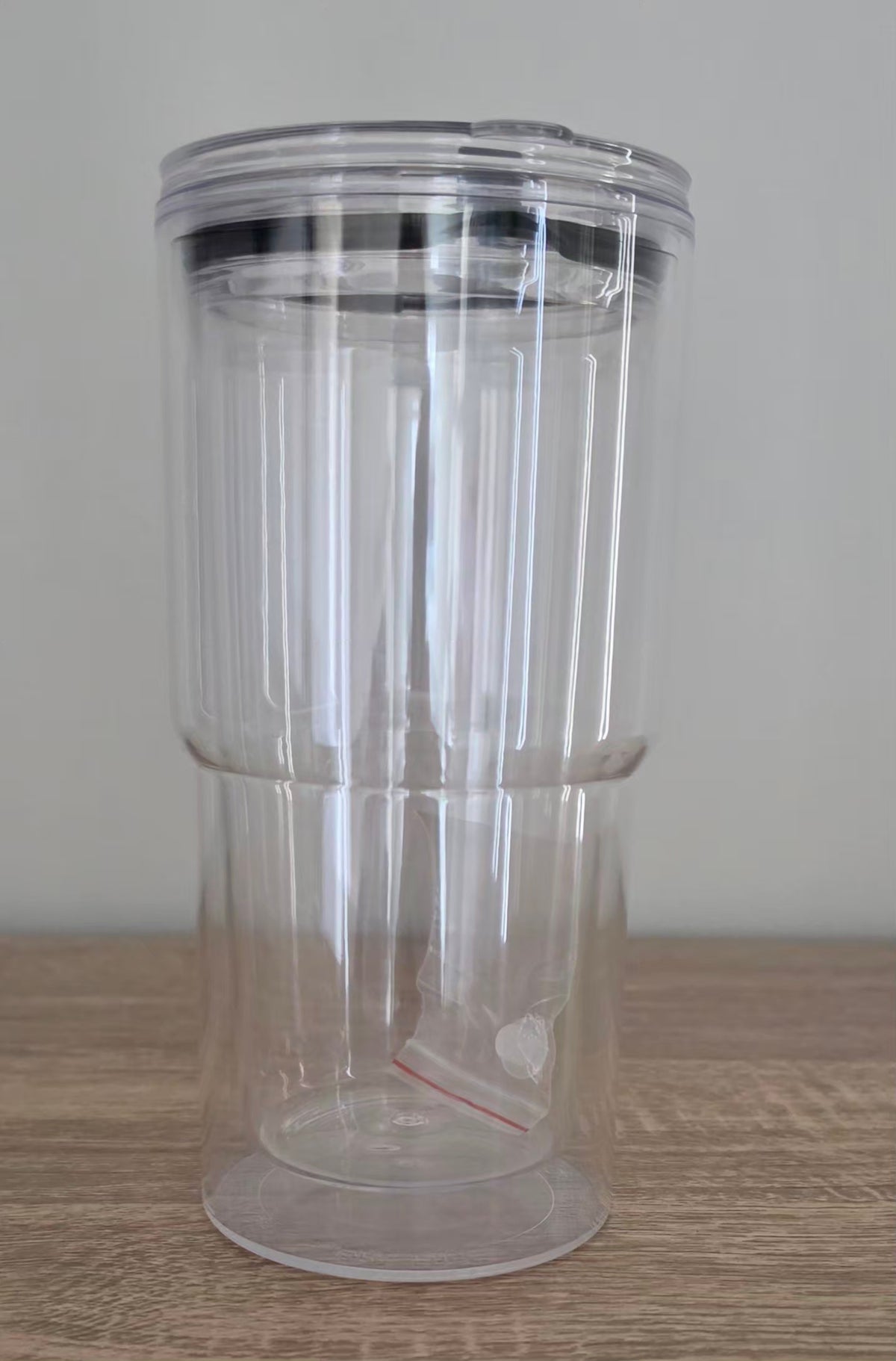 A clear plastic travel tumbler with a transparent lid and a black rim, shown on a light wood surface against a neutral gray background.
BH Creations By Mel